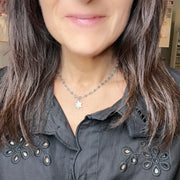 Person wearing a necklace with a star pendant, close-up of the neck and shoulders.