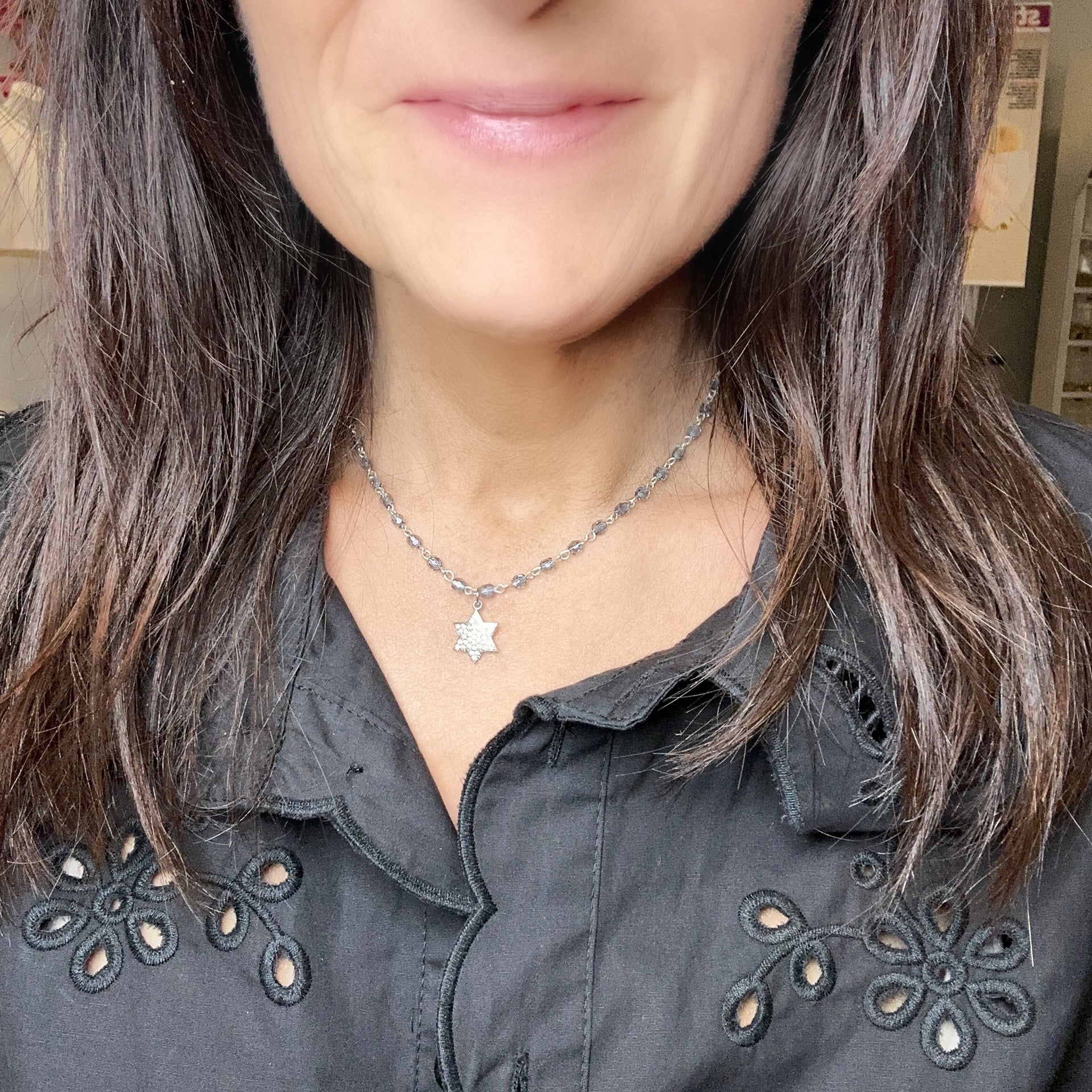 Person wearing a necklace with a star pendant, close-up of the neck and shoulders.