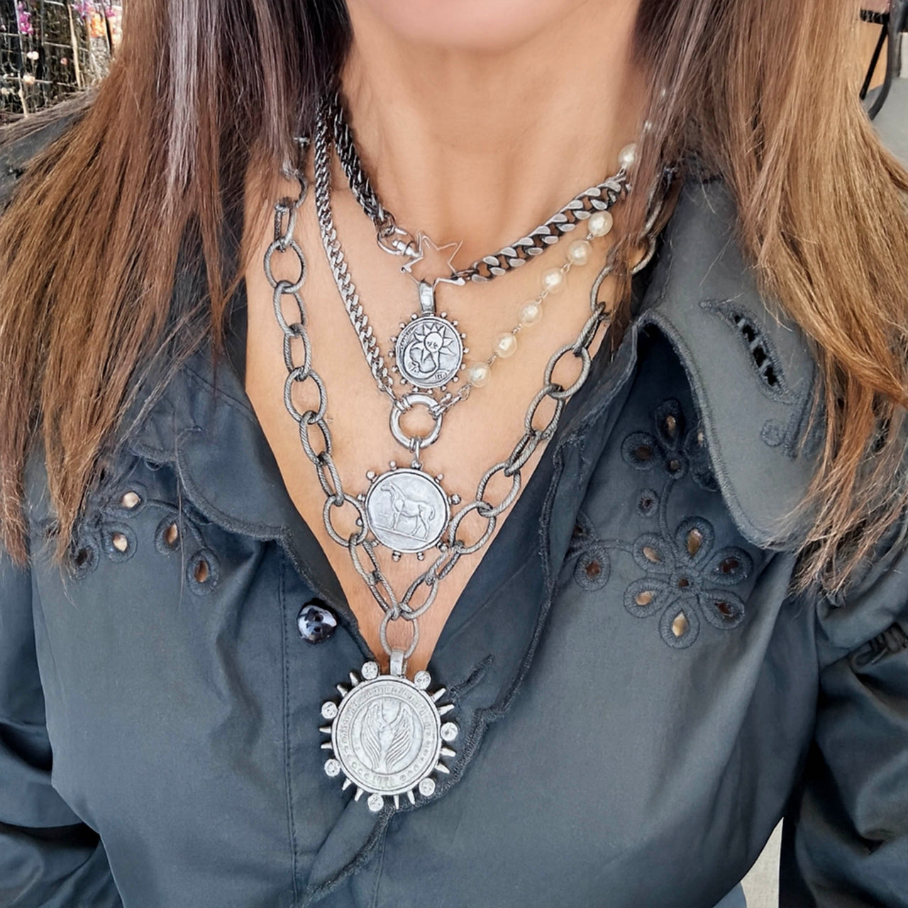 Person wearing multiple necklaces with detailed pendants on a blurred street background