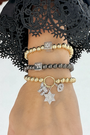 Hand wearing multiple bracelets with charms against a neutral background