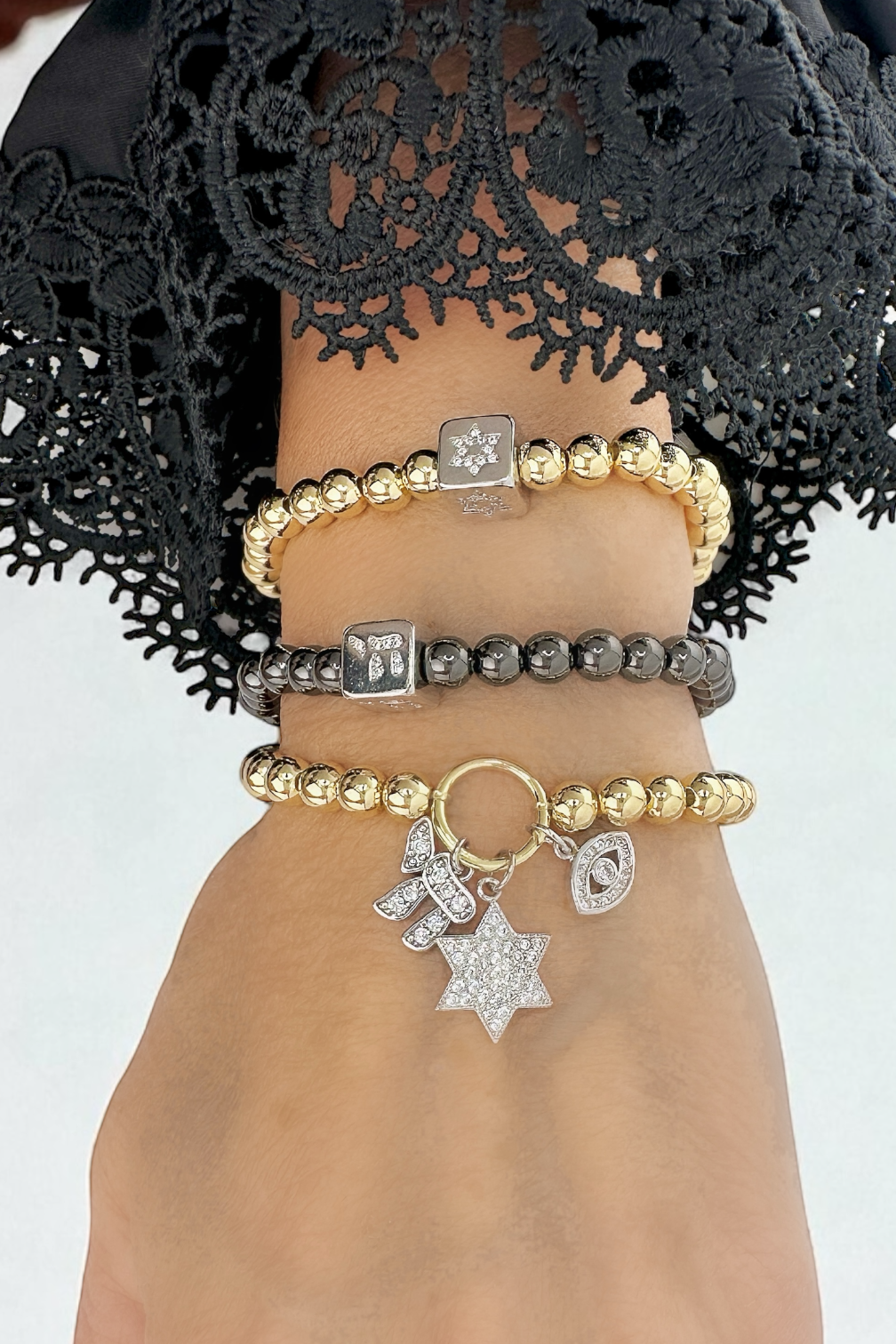 Hand wearing multiple bracelets with charms against a neutral background