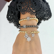 Elegant charm bracelets with gold and silver beaded designs featuring a Star of David, Chai symbol, and evil eye on a woman’s wrist with a black lace sleeve