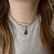 Close-up of blue enamel Hamsa charm on a gold chain necklace