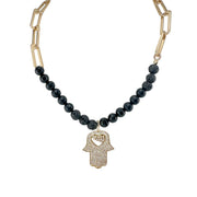 Necklace with black beads and gold Hamsa hand pendant on a white background