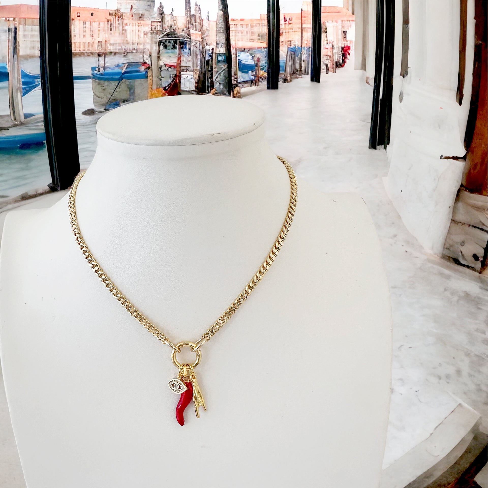 gold mariano italian protection charm necklace displayed on stand with cornicello evil eye and mano charms