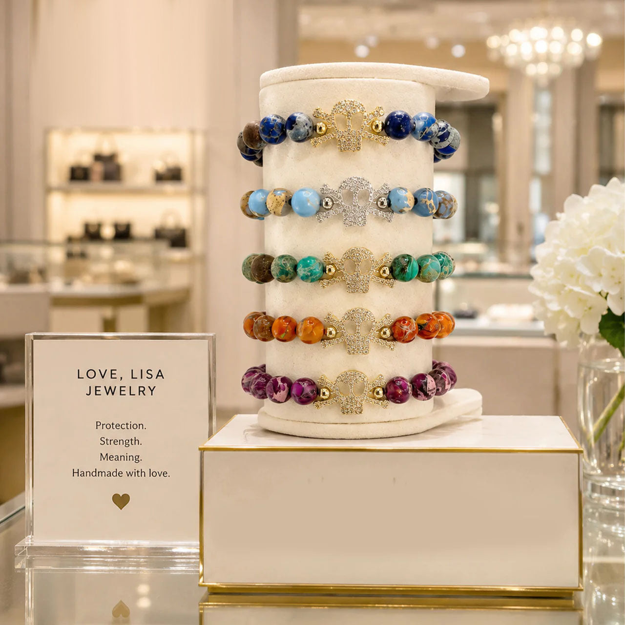 A display stand showcasing five colorful beaded bracelets with silver-toned filigree and gold-toned bead accents, set in a luxury jewelry store next to a sign for 'Love, Lisa Jewelry'.