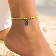 Gold anklet with a silver charm on a person's ankle against a blurred beach background
