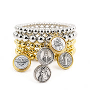 Stack of gold and silver beaded bracelets with religious charms on a white background