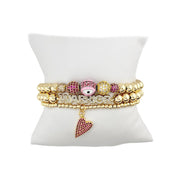 Love Lisa Meghan Breast Cancer Awareness WARRIOR Bracelet Stack displayed on white pillow with gold-tone beads, pink accents, evil eye bracelet, and slanted heart bracelet