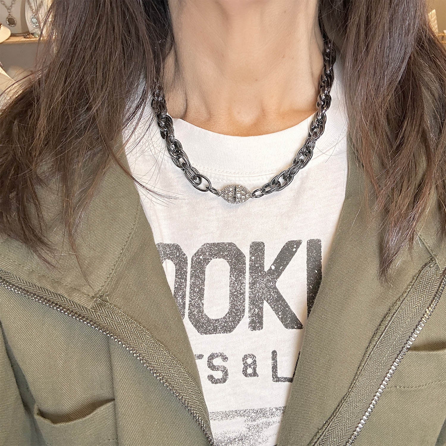 A gunmetal chain necklace with textured links and a pavé crystal magnetic clasp on model