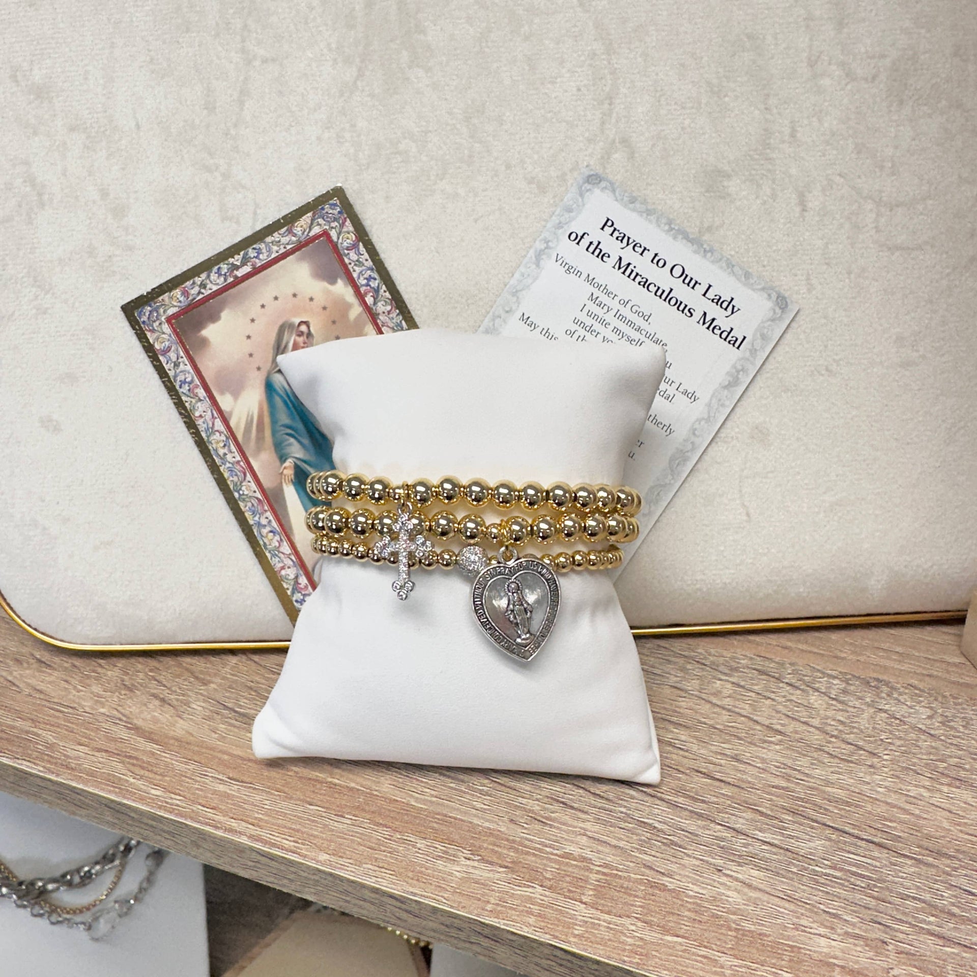 Gold and silver bracelet on a white pillow with a religious card in the background