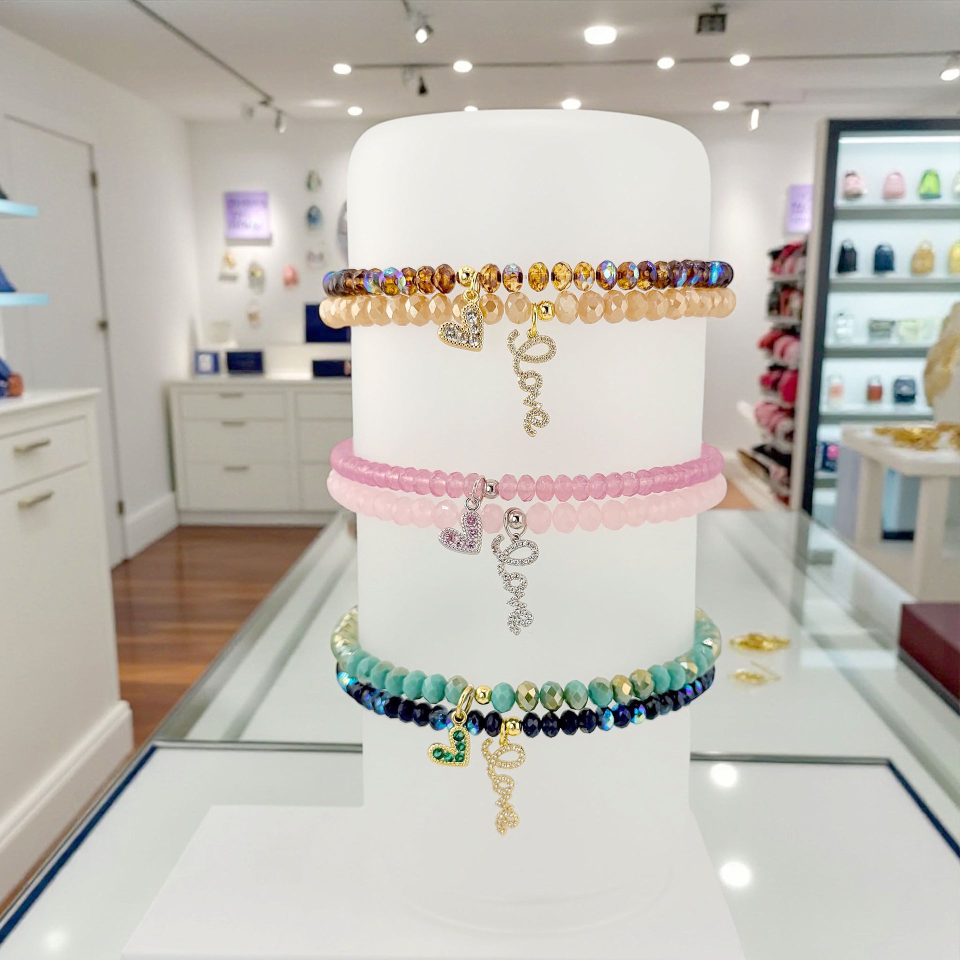 Stack of colorful beaded bracelets on a white cylindrical stand in a store setting.
