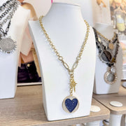 Necklace with a blue heart pendant on a white stand with other jewelry in the background.