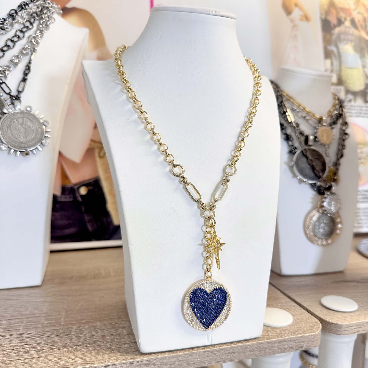 Necklace with a blue heart pendant on a white stand with other jewelry in the background.