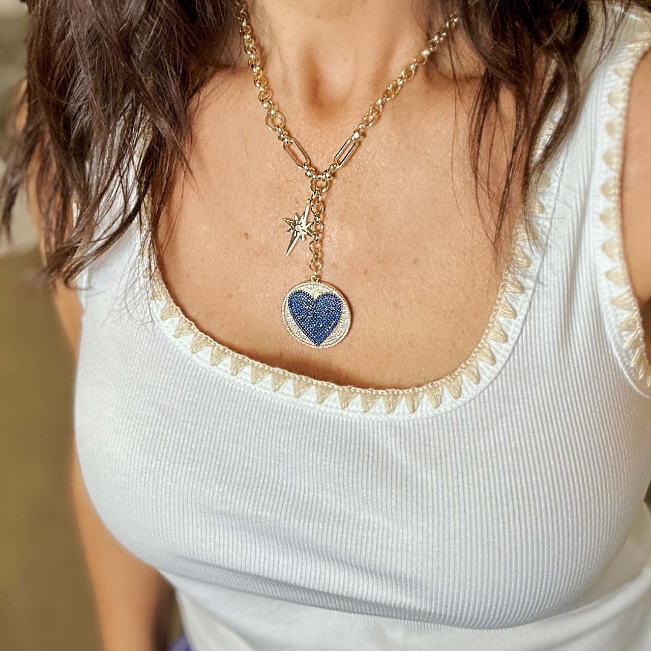 Necklace with a blue heart pendant worn by a person in a white top.
