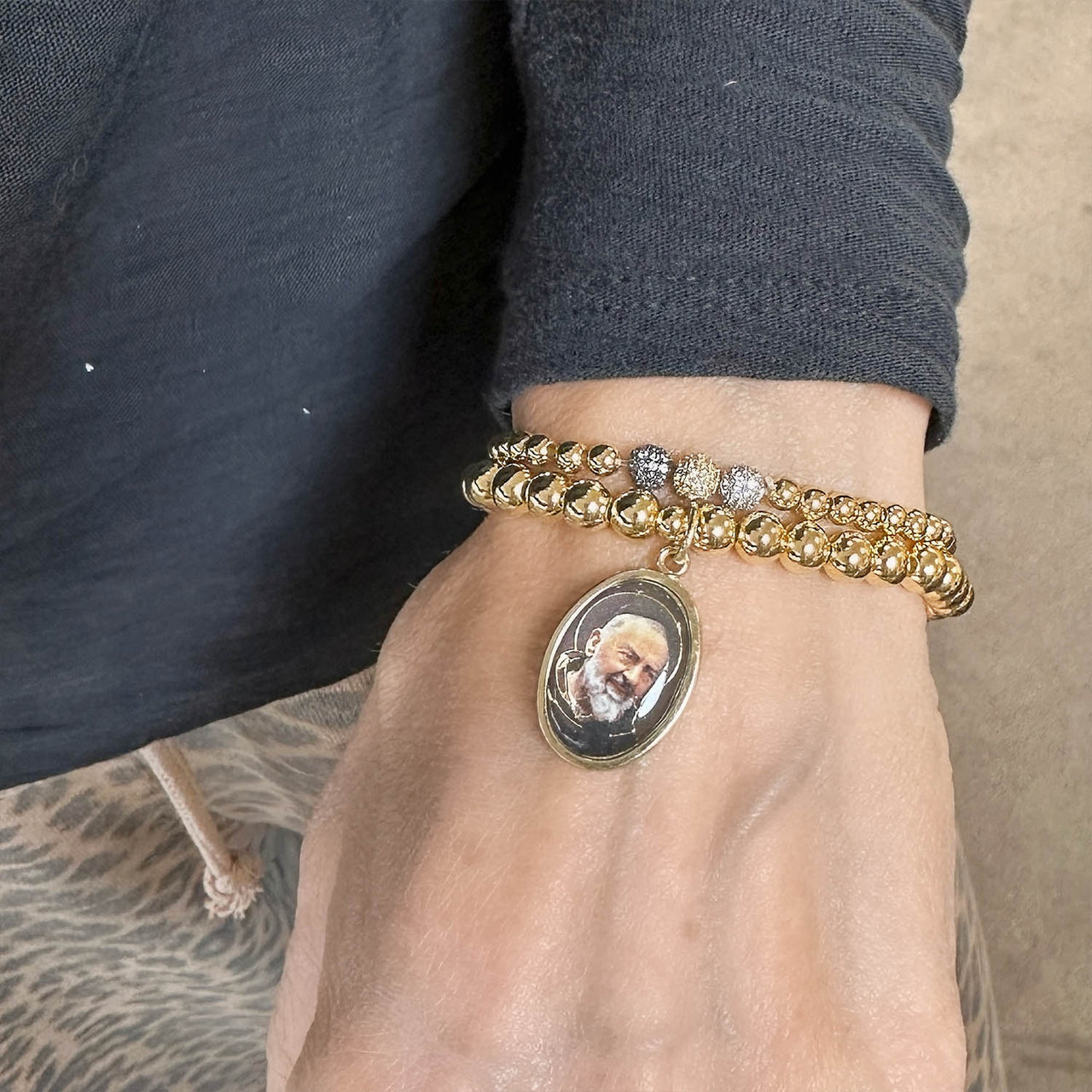 Gold bracelet with a pendant on a wrist against a neutral background