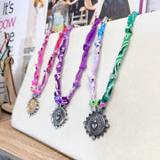 Paloma bandana coin necklaces displayed on jewelry stand with heart pendants and evil eye beads