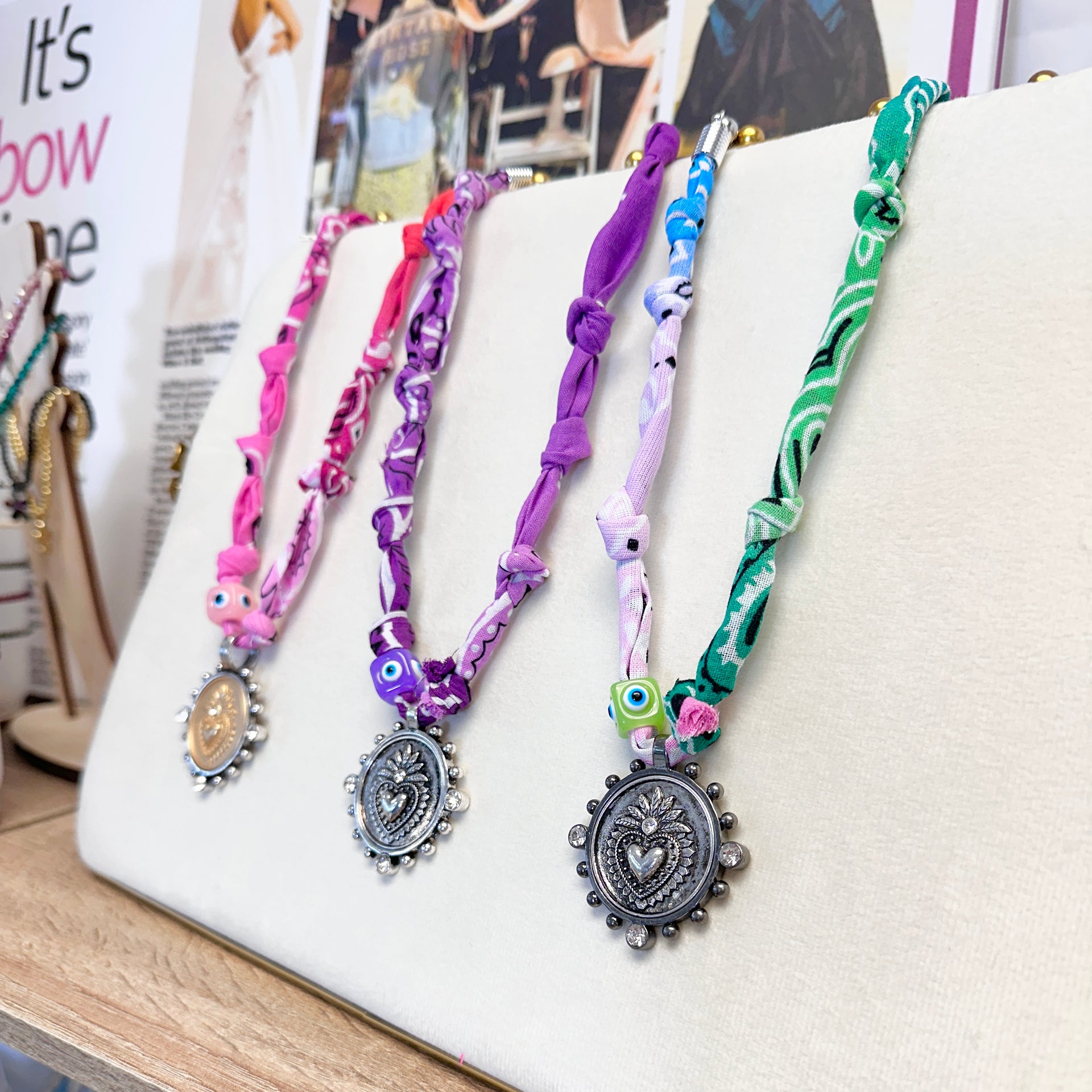 Paloma bandana coin necklaces displayed on jewelry stand with heart pendants and evil eye beads