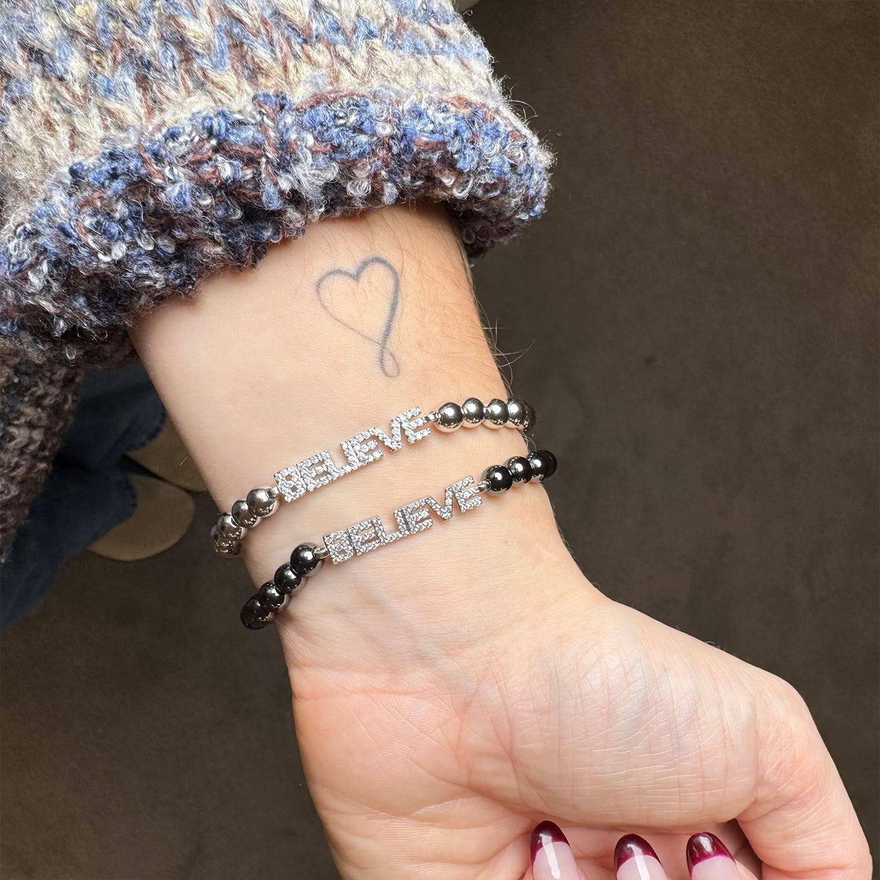 believe bracelet on a wrist with a heart tattoo
