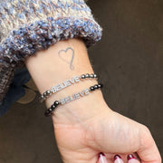 believe bracelet on a wrist with a heart tattoo