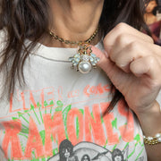 Person wearing a necklace with a large pearl pendant, pointing to it, on a Ramones t-shirt.