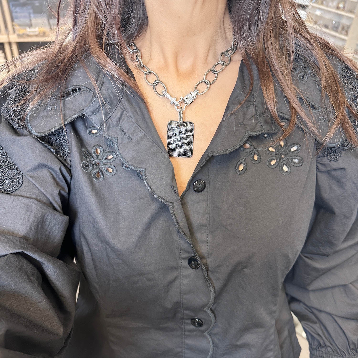 Person wearing a dark gray button-up shirt with decorative collar and a necklace with a pendant.
