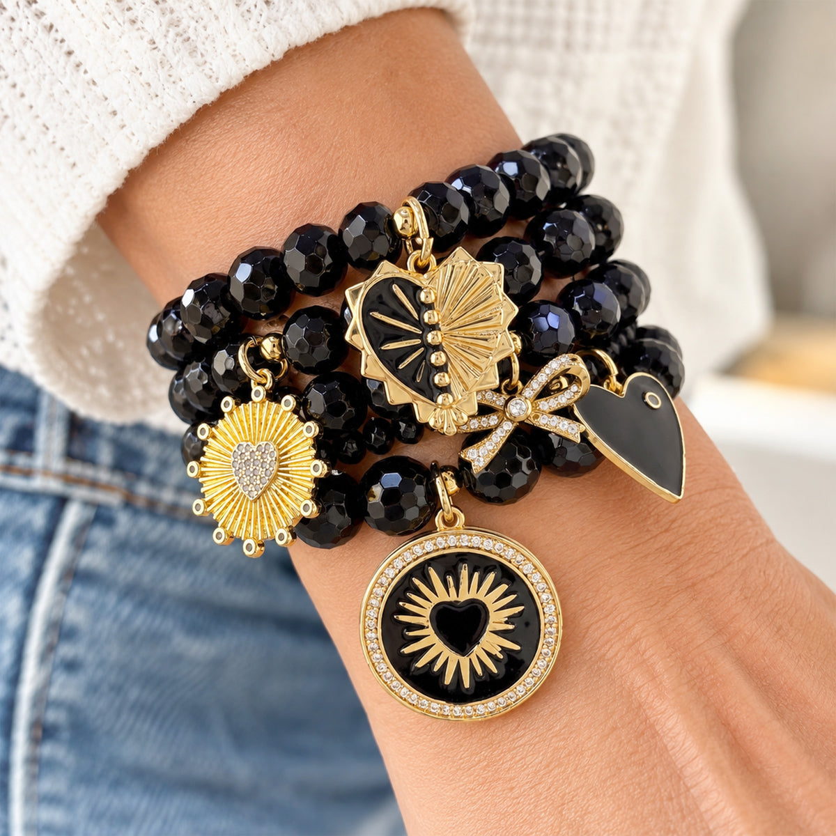 Love Lisa Remi Heart Charm Bracelet Stack worn on wrist with layered faceted black onyx beads, gold-tone heart medallions, black enamel accents, pavé bow, and crystal details