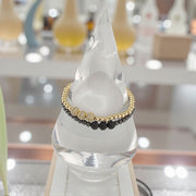 Bracelet with gold and black beads on a clear stand with blurred background