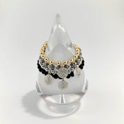 Multistrand bracelet with gold, silver, and black beads on a clear stand against a white background
