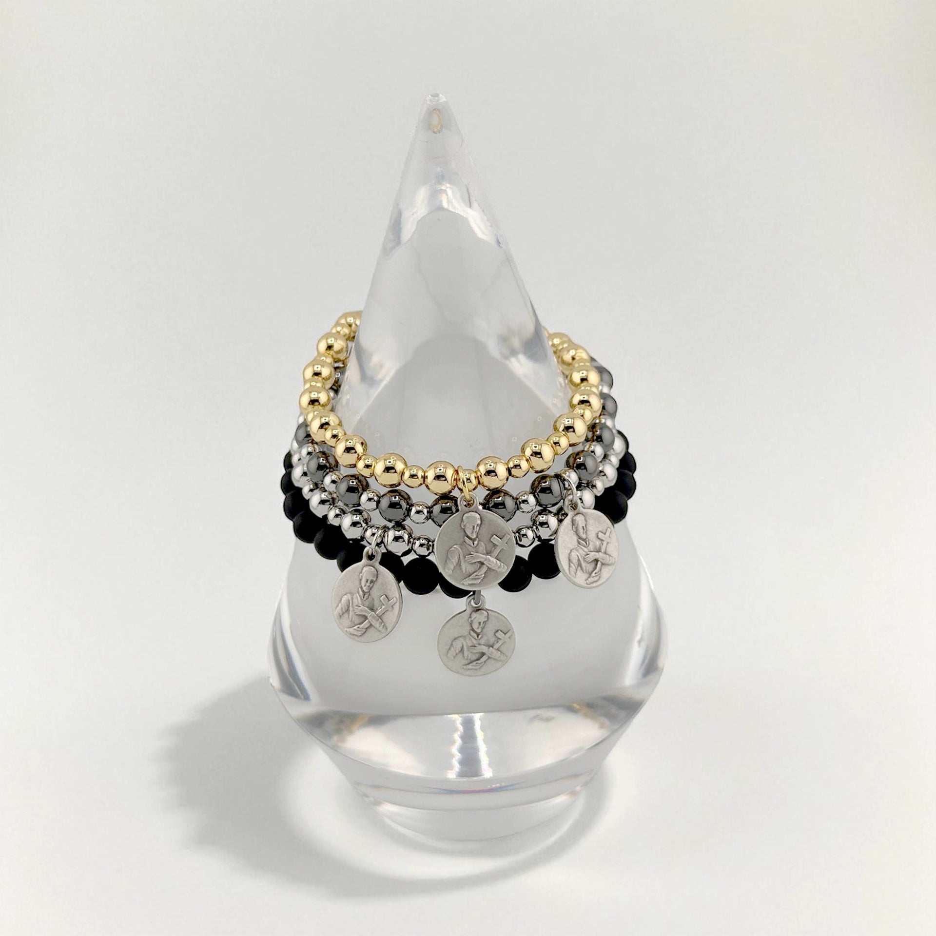 Multistrand bracelet with gold, silver, and black beads on a clear stand against a white background