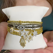 Stack of gold and silver bracelets with charms on a white cushion held by a person.