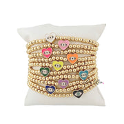 A collection of beaded bracelets with gold-colored beads and multicolored heart charms displayed on a white surface.