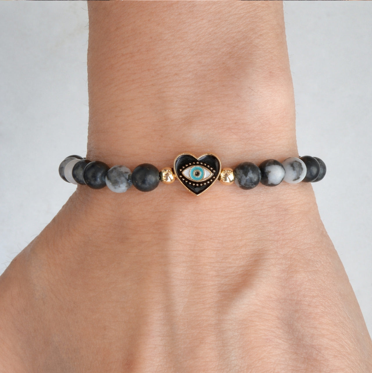 Sandi heart evil eye gemstone stretch bracelet with black and gray marbled beads and gold accents worn on wrist