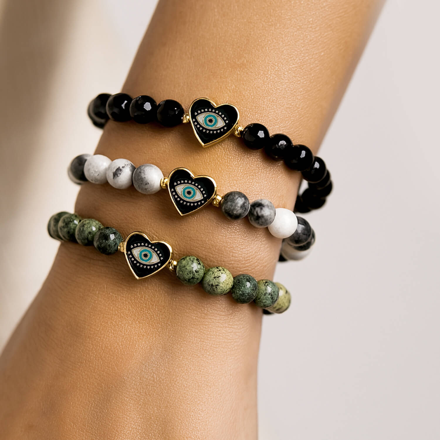 Stack of three beaded bracelets with heart-shaped eye charms on a wrist against a neutral background