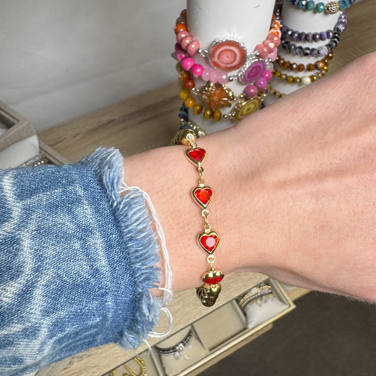 Close-up of a wrist wearing a red heart bracelet with colorful beaded bracelets in the background.