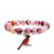 A beaded stretch bracelet featuring marbled pink, red, and white beads, with a dangling cardinal bird charm in red and black on a silver-toned clasp, shown on a plain white background.