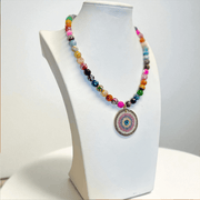 Colorful fire agate gemstone beaded necklace with a round pavé evil eye pendant in pink blue and silver displayed on a white jewelry bust