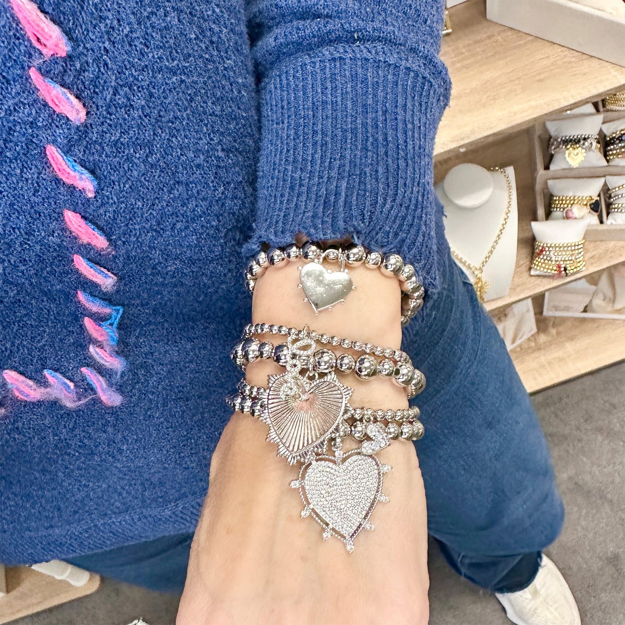 Model is wearing 5 stretch bracelets with mixed gold beads and three heart charms: pavé crystal heart, polished heart, and sunburst heart. 