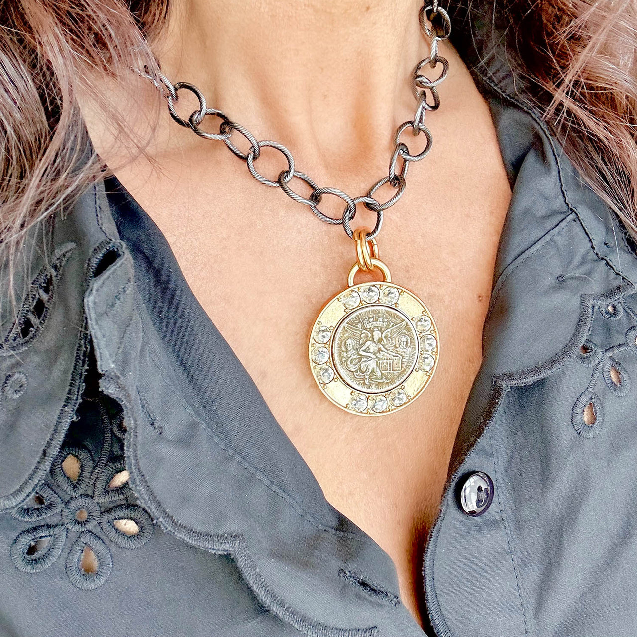Gold necklace with a decorative pendant worn by a person against a gray shirt background