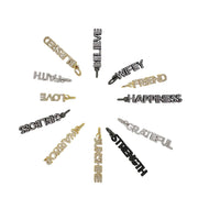 A collection of crystal-encrusted charms with various positive words written on them, such as Strength, Love, and Happiness, in gold, silver, and black colors.
