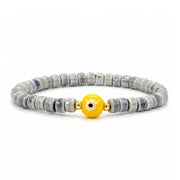 A beaded stretch bracelet featuring gray and white marbled stone beads with a central yellow evil eye charm, flanked by small gold spacer beads, on a white background.