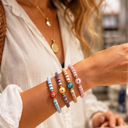 Woman wearing pink ceramic evil eye bracelet stacked with colorful beaded bracelets