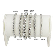 A series of six silver beaded bracelets stacked together, featuring a variety of round beads.