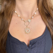 Necklace with sun-shaped pendant and pearl accents on a person's neck.