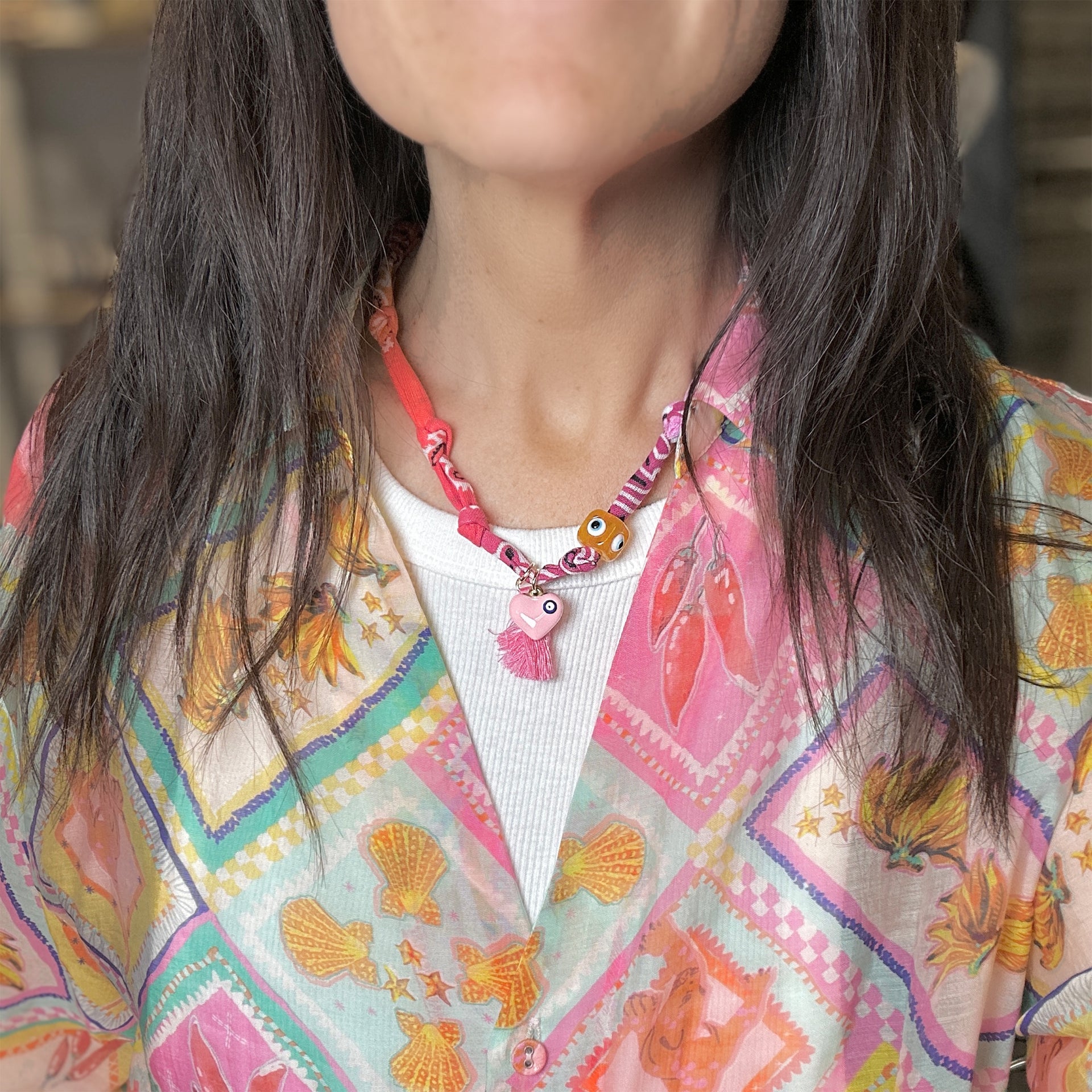 Person wearing a colorful patterned jacket with a necklace featuring tassels and beads.