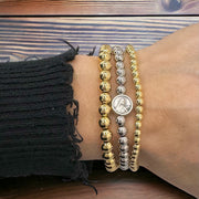 
Stacked gold and silver beaded bracelets with St. Therese charm shown on wrist
