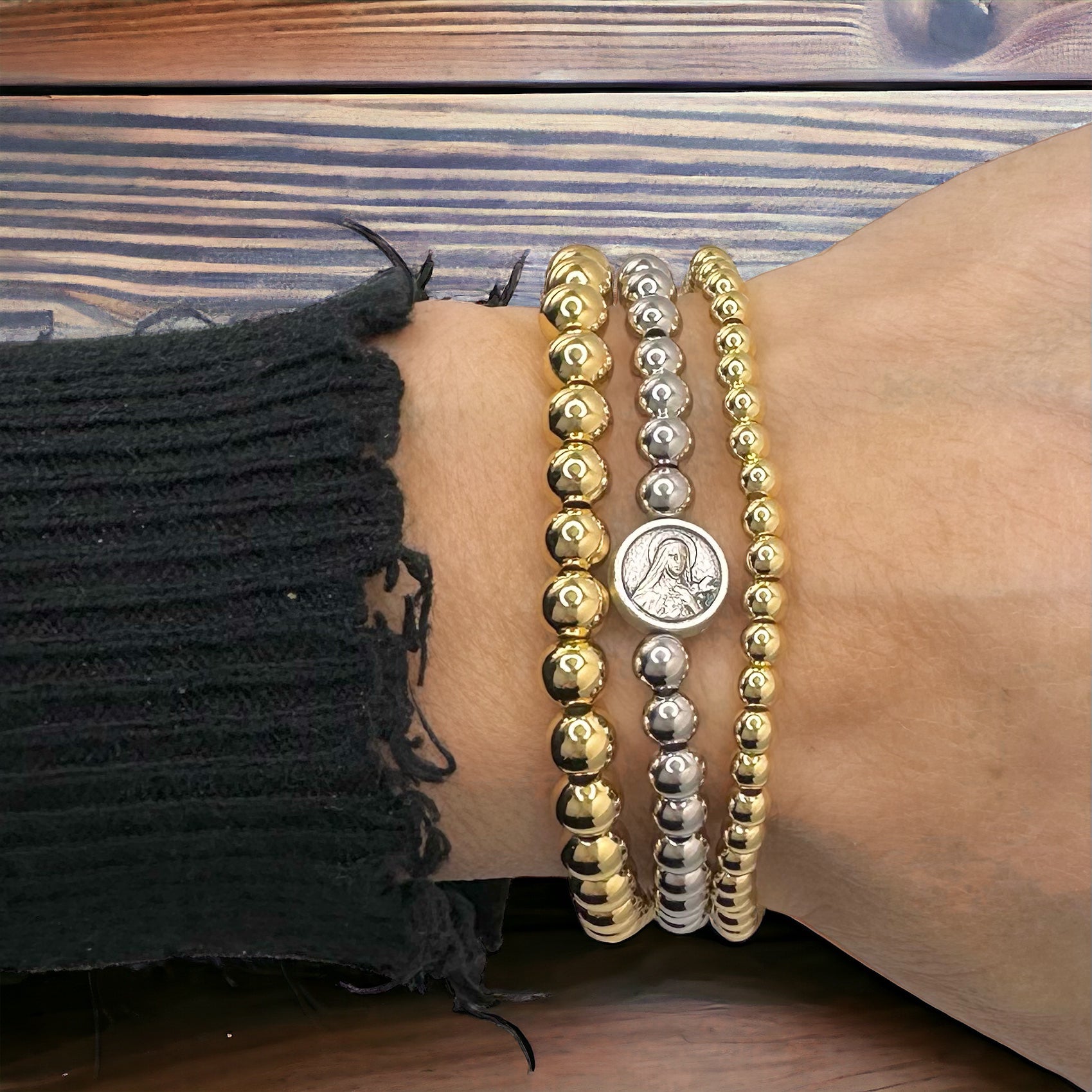 
Stacked gold and silver beaded bracelets with St. Therese charm shown on wrist