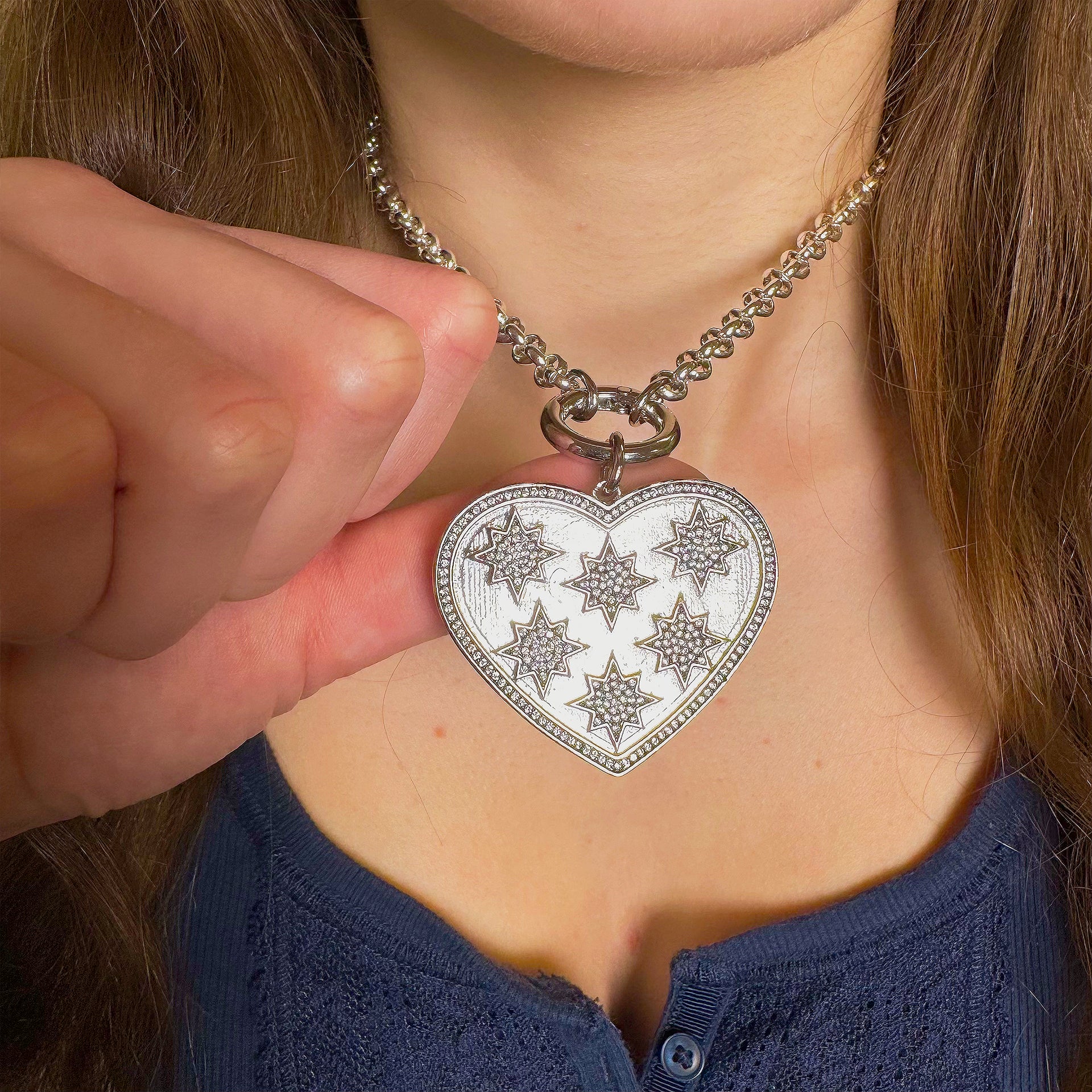 Person wearing a silver heart-shaped necklace with star designs.