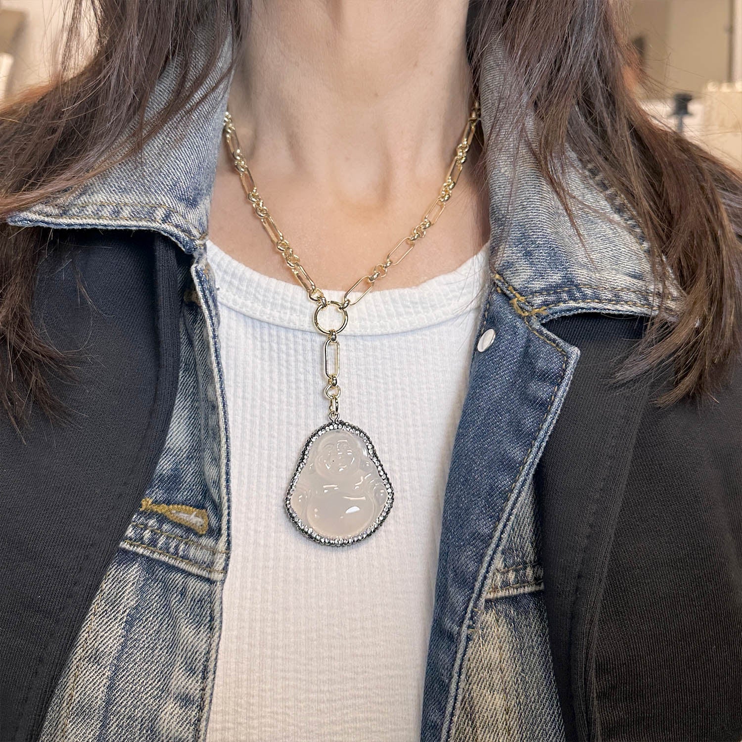 Person wearing a necklace with a pendant, dressed in a denim jacket and white top.