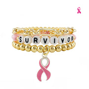 Love Lisa Survivor Breast Cancer Awareness Bracelet Stack in gold with SURVIVOR bead detail, paperclip chain, polished beads, pink enamel ribbon charm, and Pink Aid logo